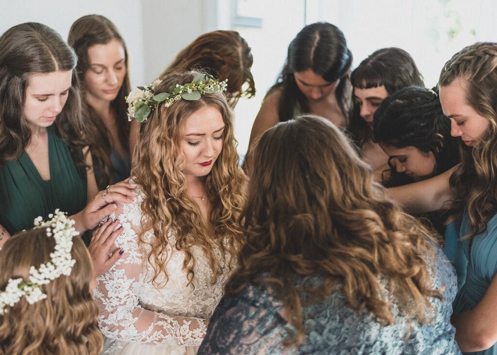 bridesmaids and mother praying over bride laying hands before Christian wedding ceremony