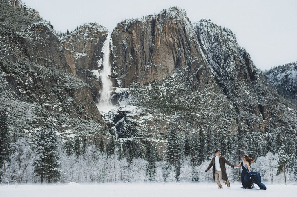 Couple running in Yosemite valley during engagement session with frozen waterfall