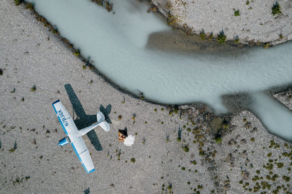 Aerial view of a couple beside their bush plane and a glacial river during an Alaska elopement