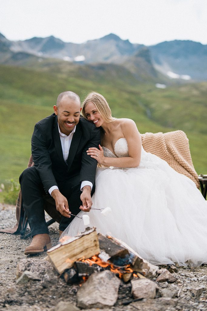 Alt: Bride and groom roasting marshmallows by a campfire during their Hatcher Pass elopement